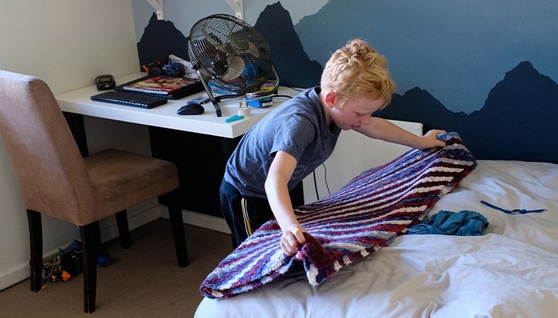 Child folding a blanket in his bedroom