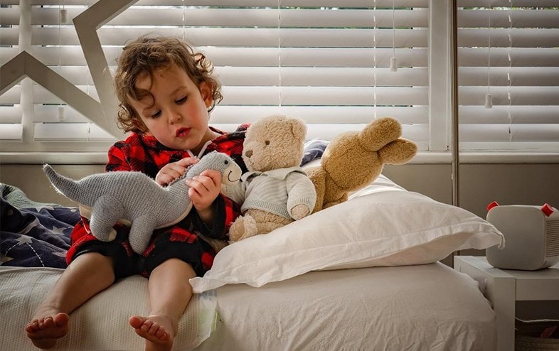 Toddler sitting in his bedroom while playing with soft toys