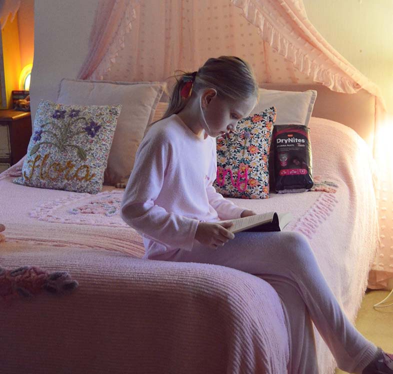 Girl in pyjamas sitting on her bed reading