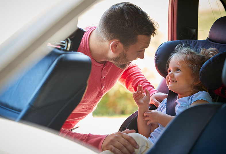 Dad securing his smiling daughter in a car seat