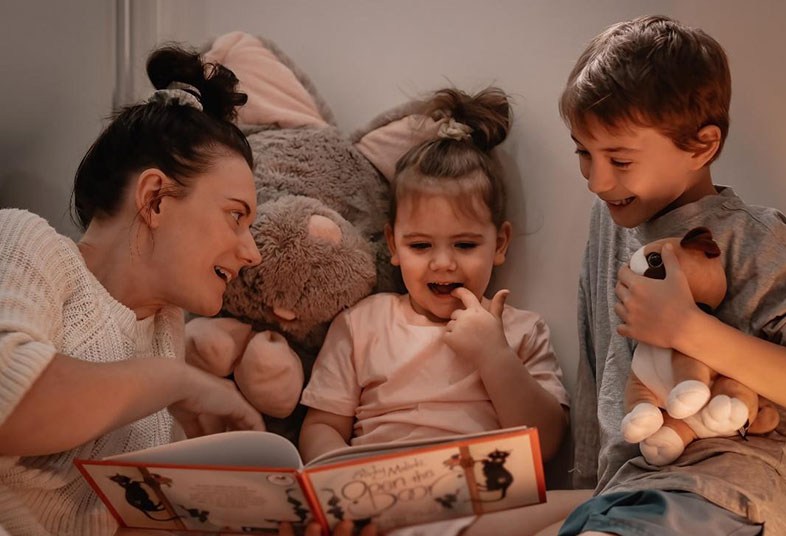 Mom lying in bed reading to her two kids