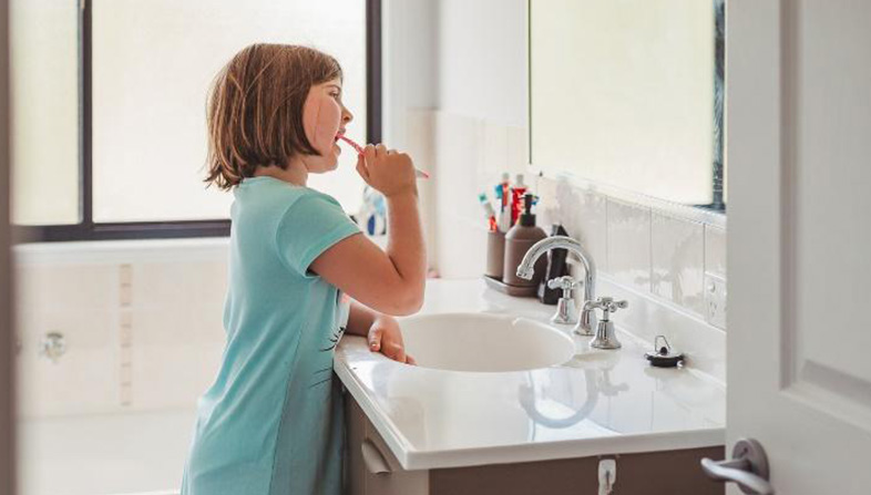 Young girl standing at a mirror brushing her teeth