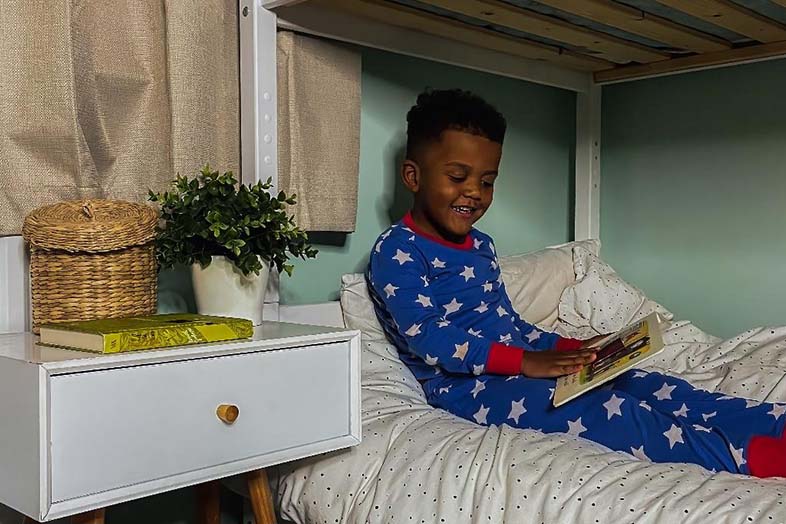 Young boy sitting in his bed reading a book