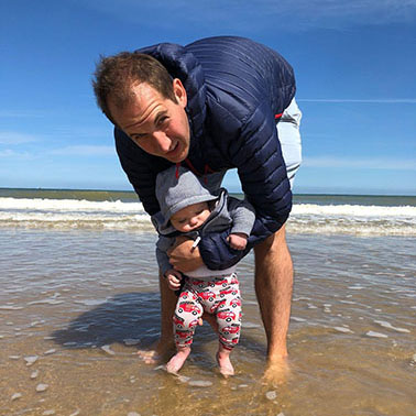 Father and baby daughter padding in sea waves.